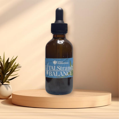 A brown glass dropper bottle labeled "Vital Strandz Balance" is placed on a wooden platform. There is a small plant to the left of the bottle, underscoring the product's focus on scalp health.